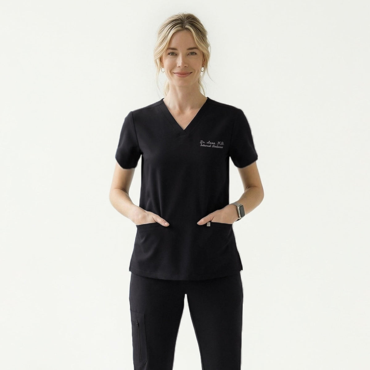 Woman wearing a black V-neck scrub top with embroidered name and double front pockets, paired with matching black scrub pants,Eco Black