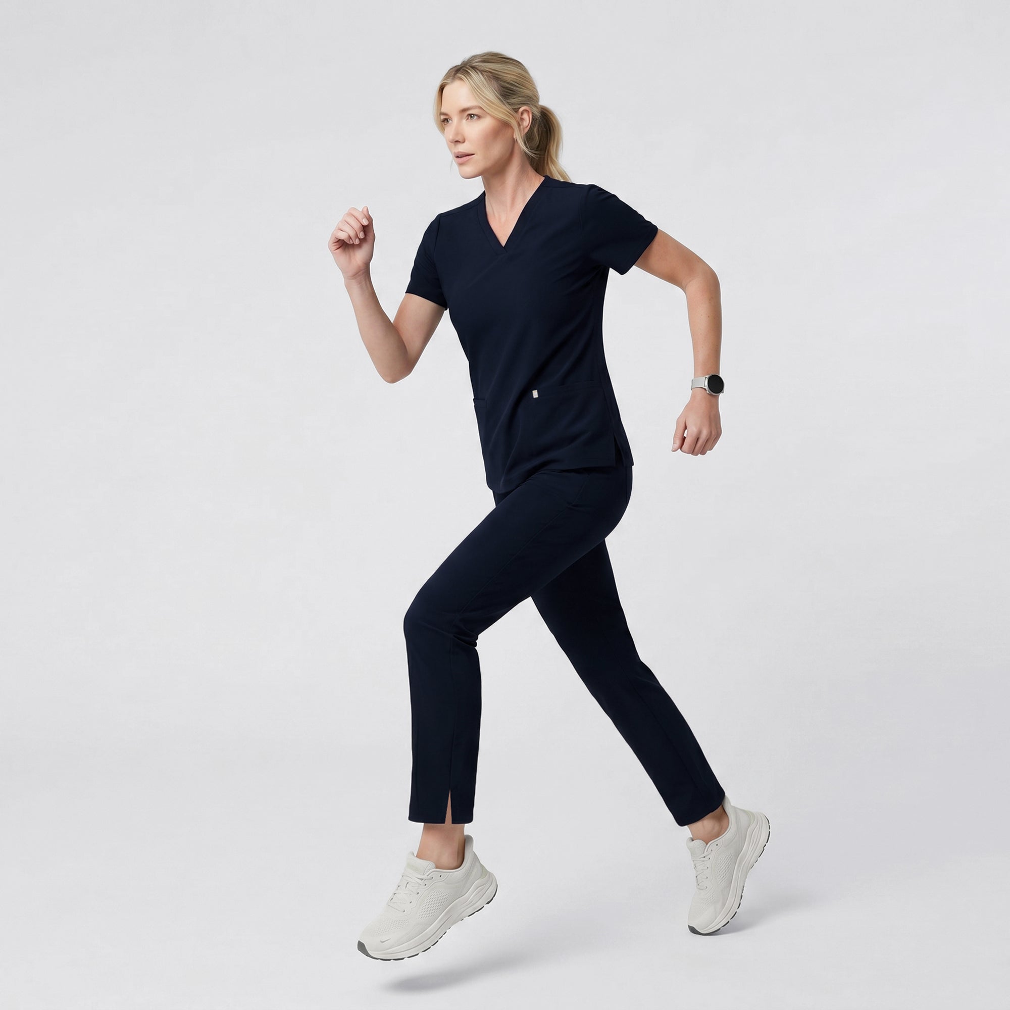Front view of a model wearing the Eco Navy Double Pocket Scrub Top with matching jogger pants.