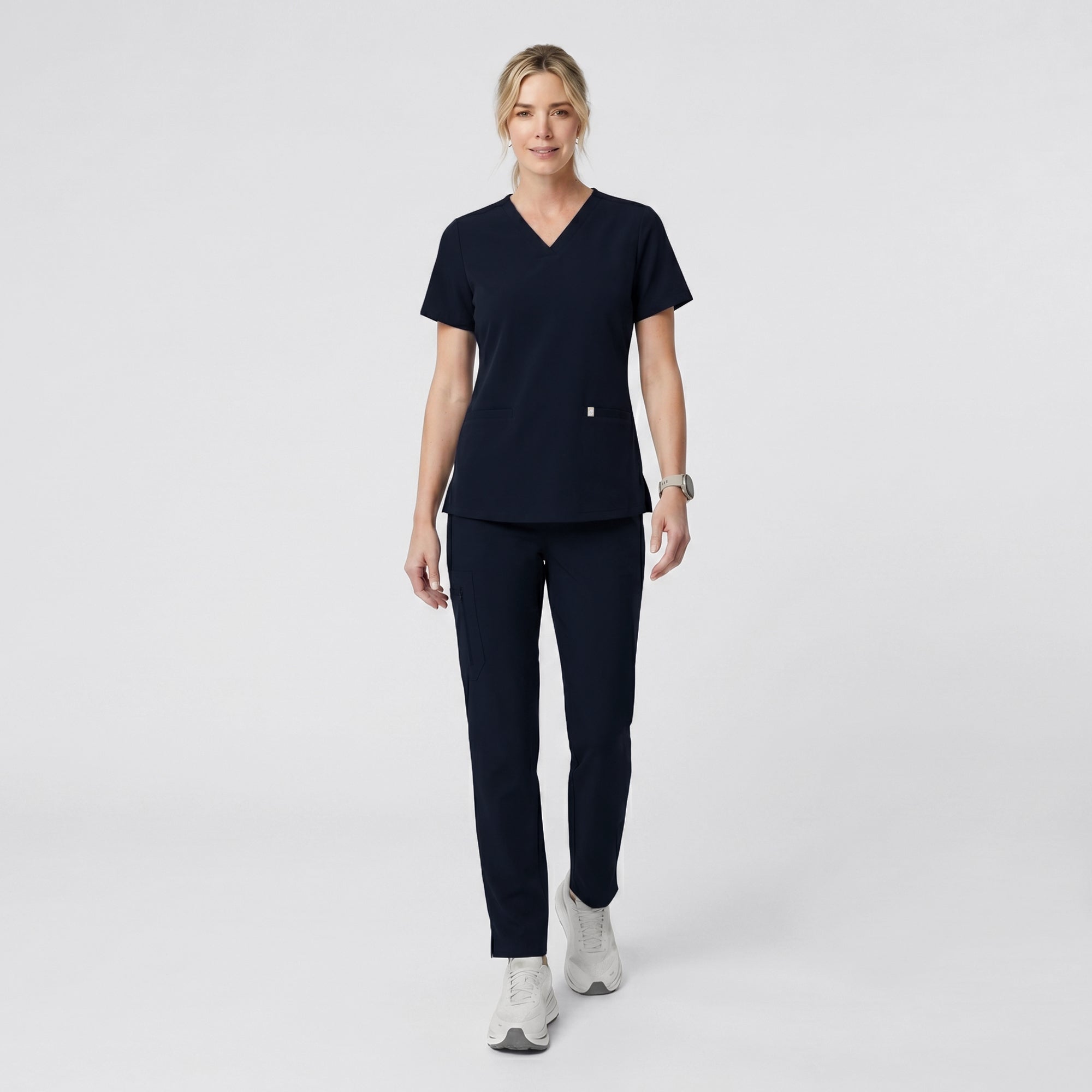Model wearing the Eco Navy Double Pocket Scrub Top and matching jogger pants, standing with hands in pockets.