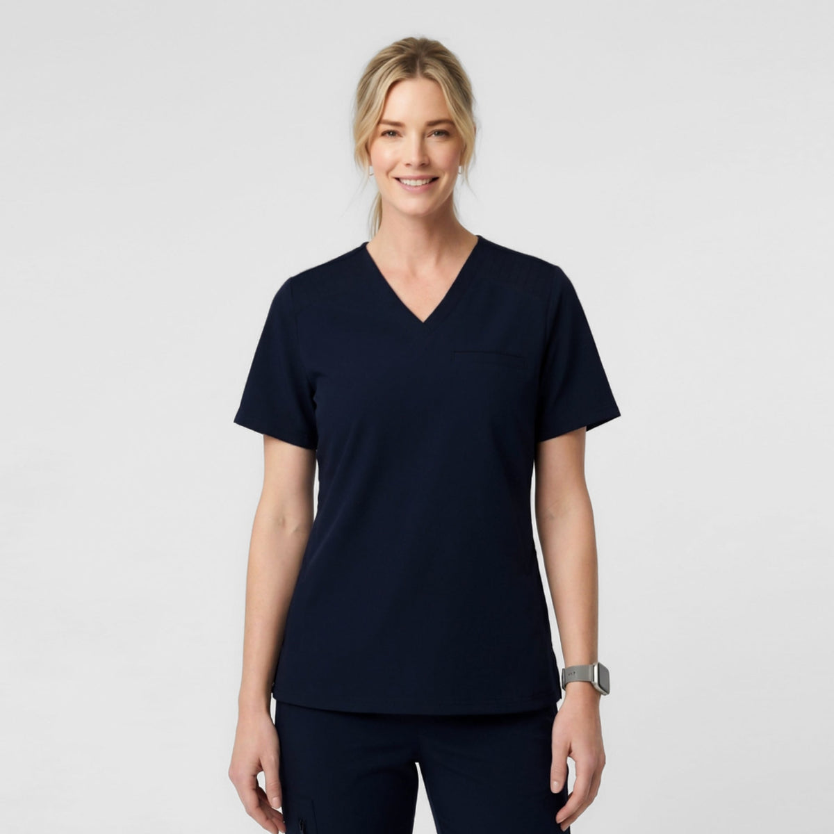 A Female model wearing Eco Navy ZenFlex scrub top with matching scrub pants.