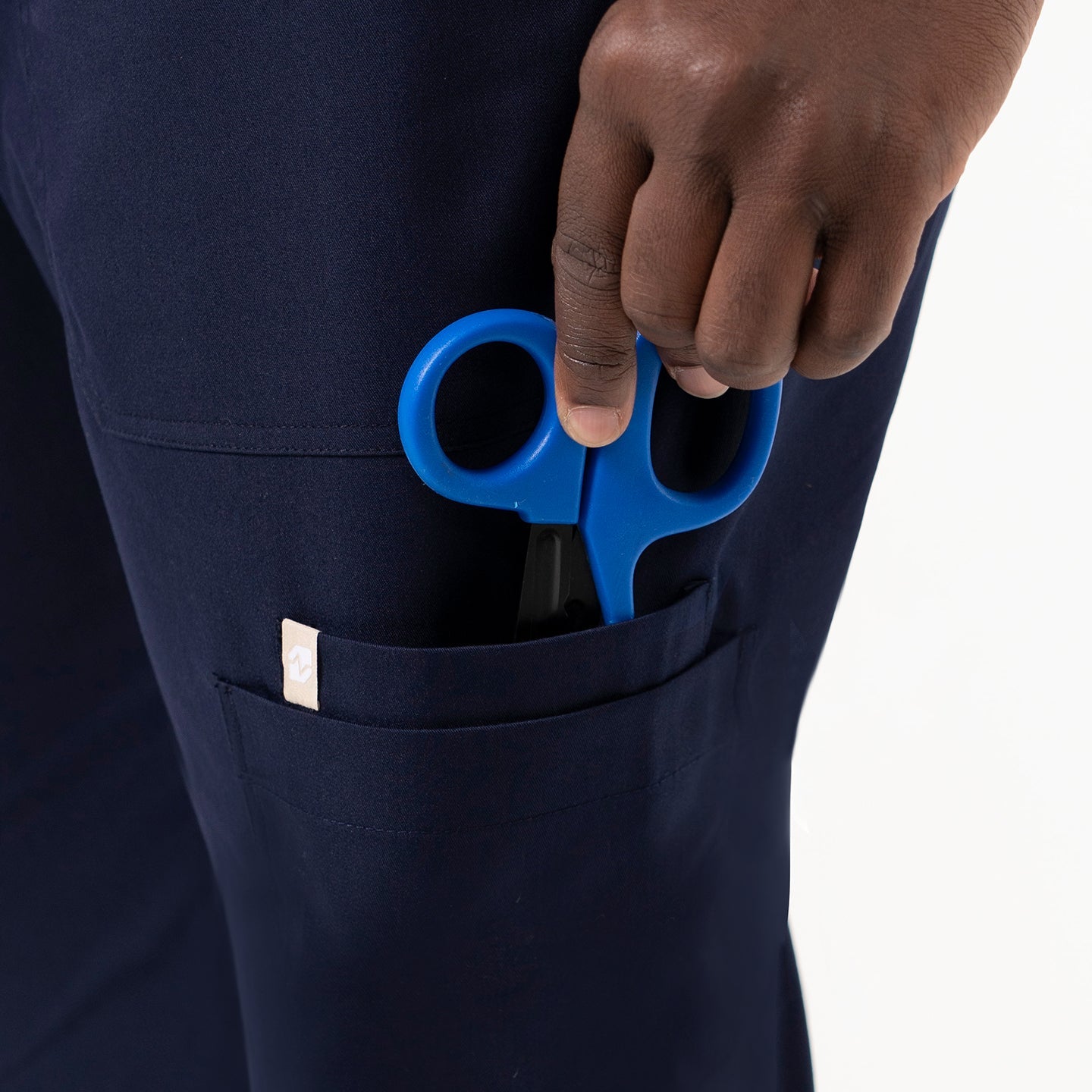 Close-up view of the 8 Pocket Jogger Scrub Pants with blue medical scissors in the side pocket.