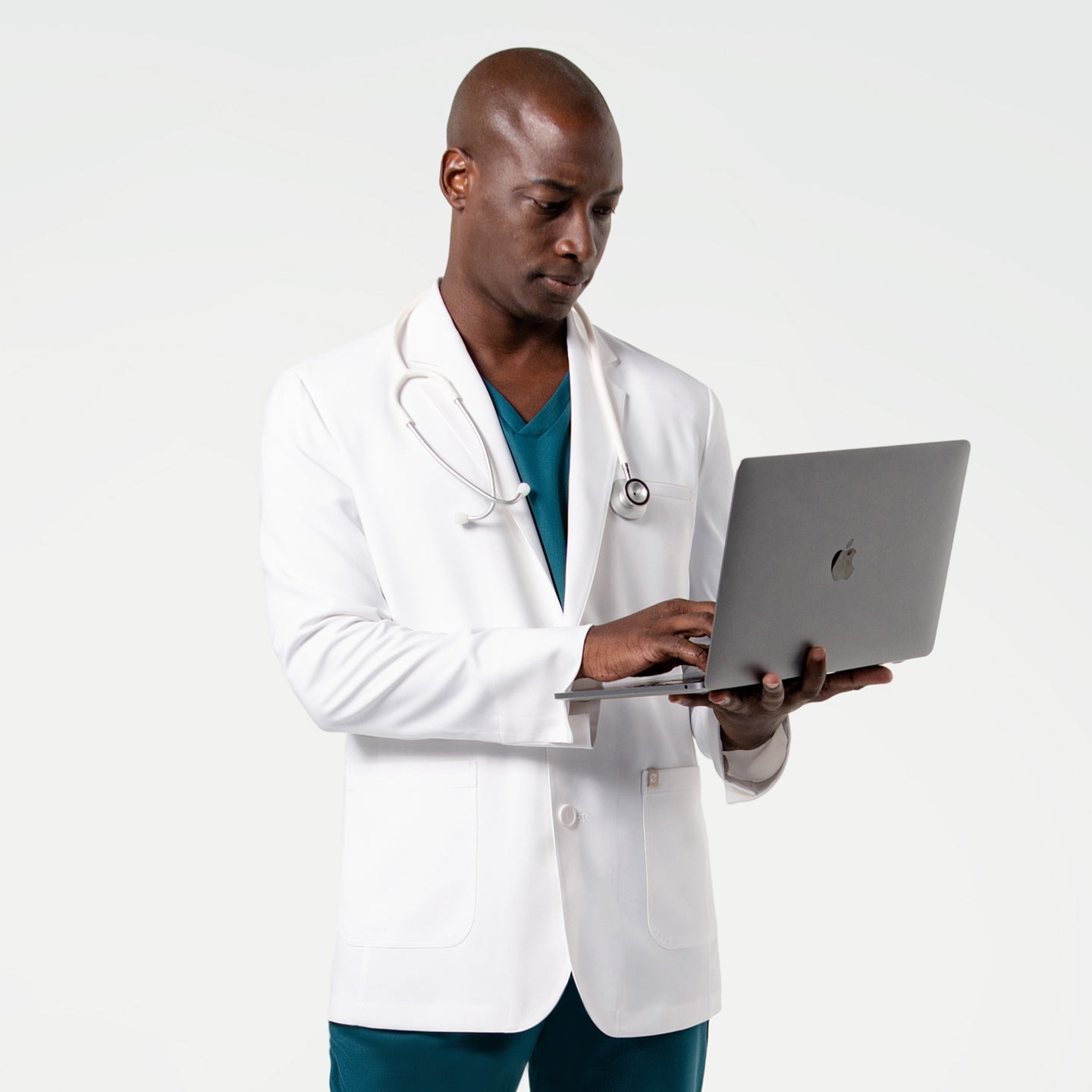 Using a laptop in the Men's LCM-102 Lab Coat in White over medical scrubs, stethoscope draped around the neck, upper body view