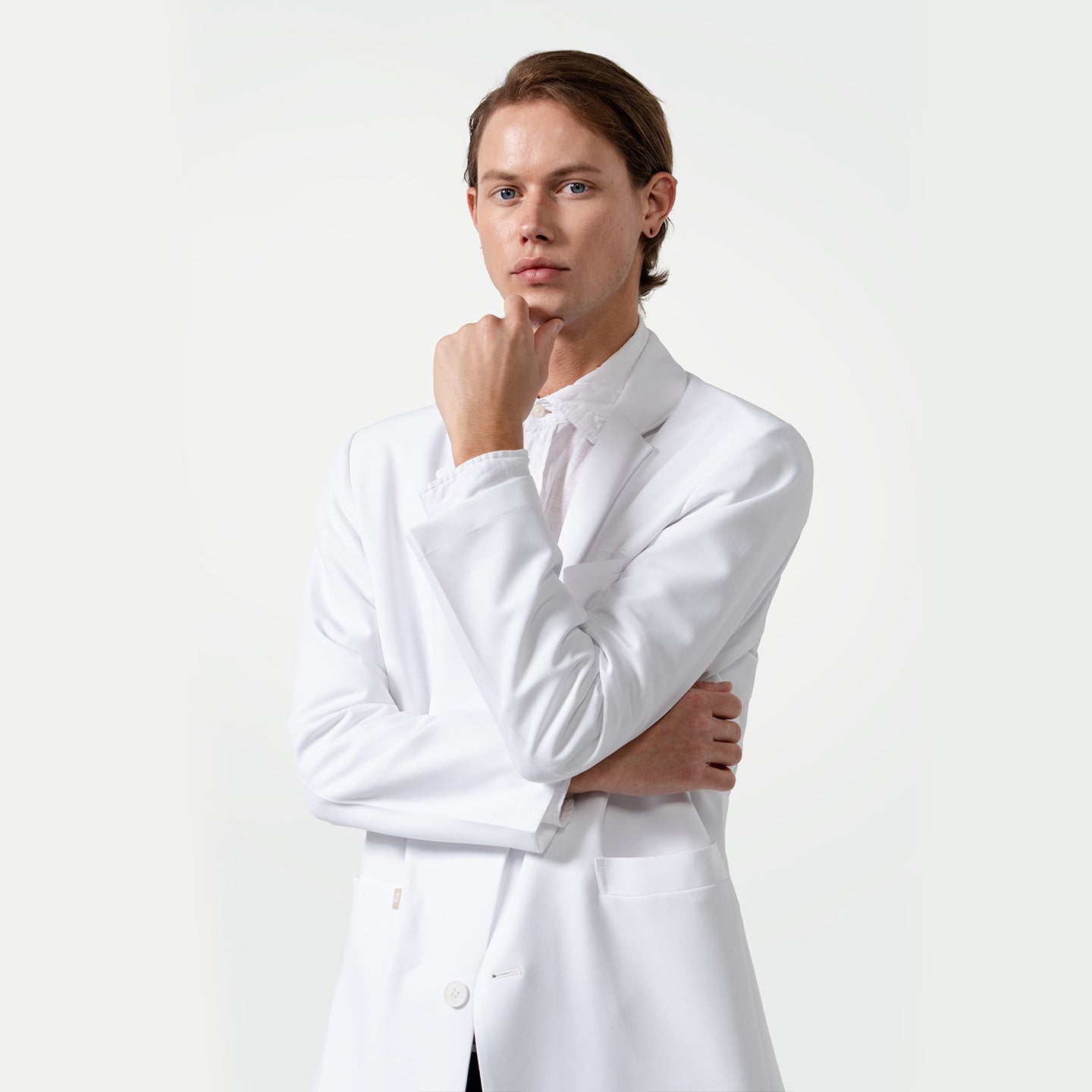 Male model wearing a white Lcm-103 lab coat over a white shirt, standing with one hand on chin and the other arm folded.