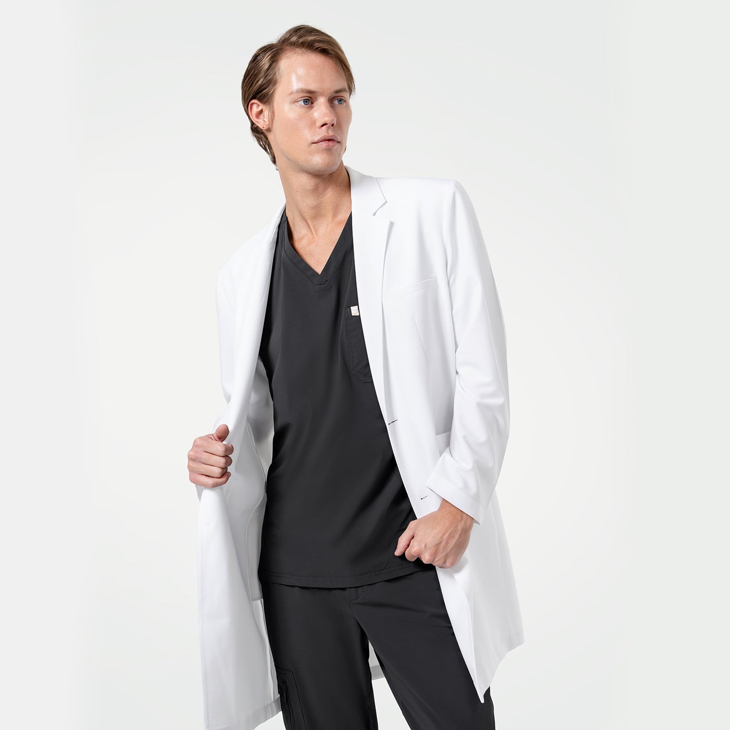 Lcm-103 men’s white lab coat styled over black scrub top and pants, model holding coat open to show inner fit, professional medical apparel on light background.