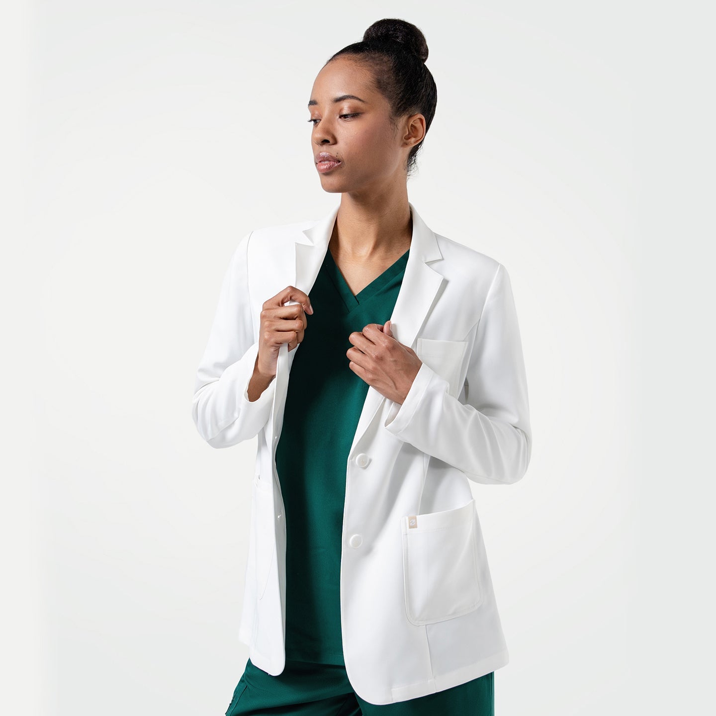 Woman holding the Women's LCW-101 Lab Coat in White over pine green scrubs, looking slightly to the side, upper body view