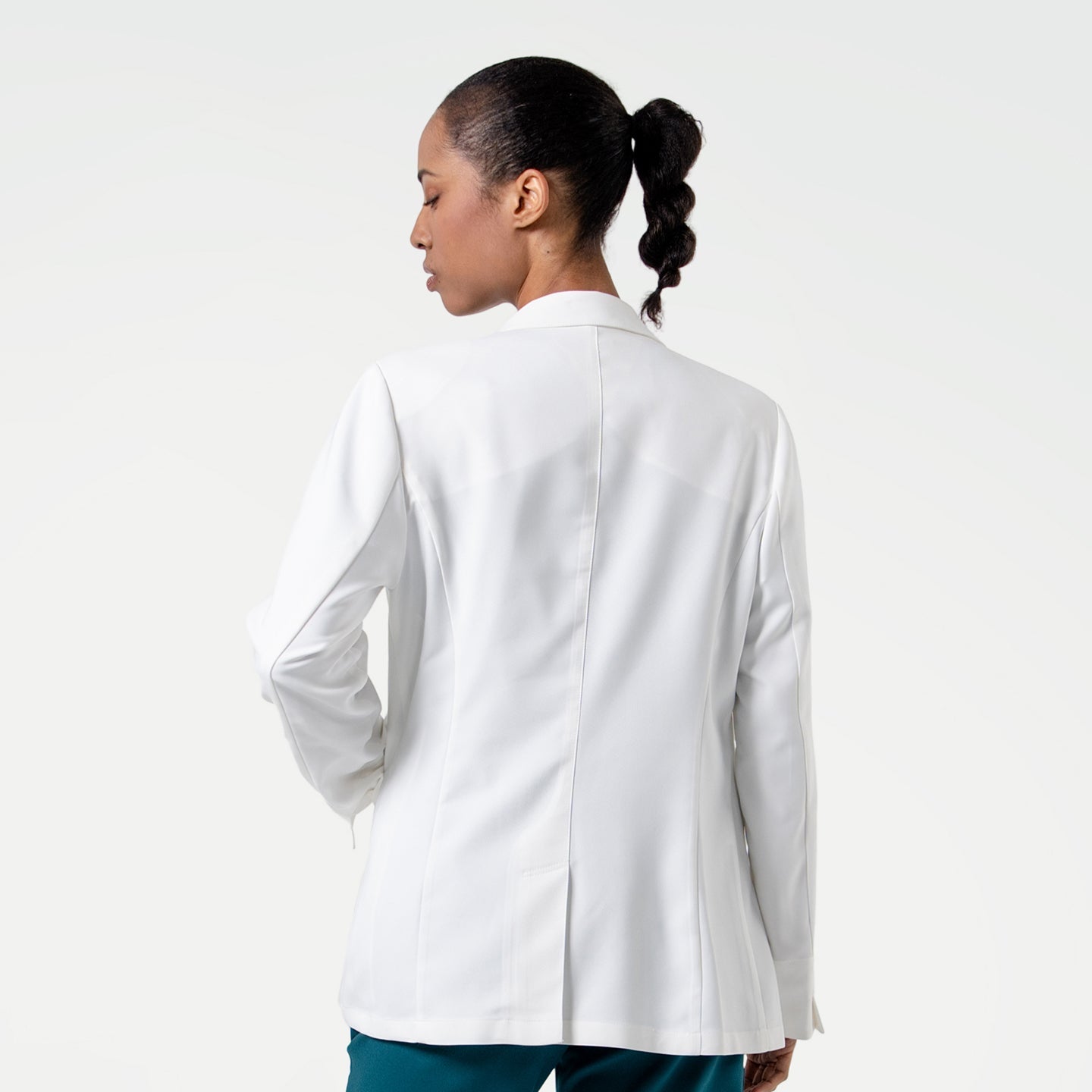 From behind, the model in the Women's LCW-04 Lab Coat in White over medical scrubs turns slightly to the side, upper body view