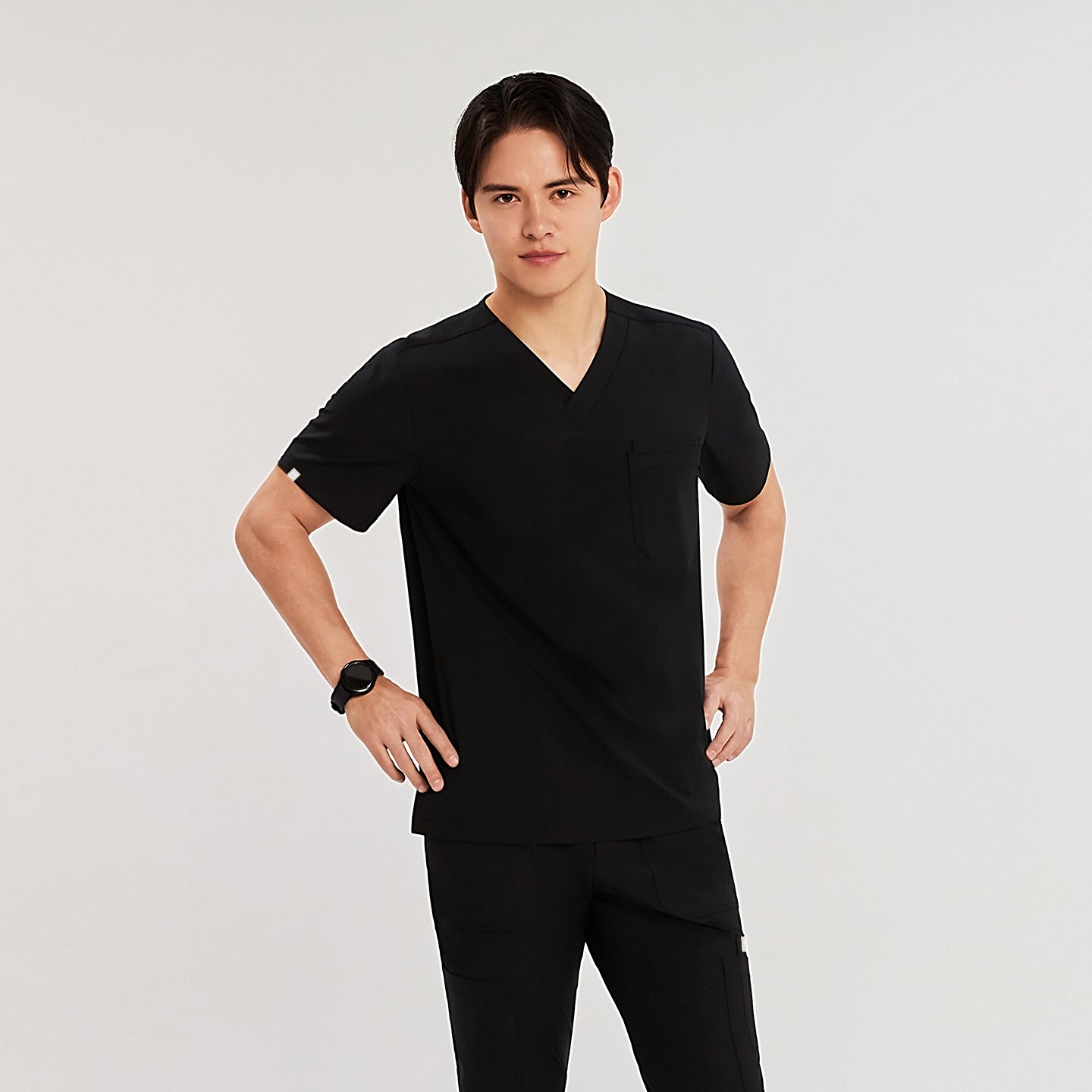 Man in black Zenir scrub top with chest pocket, standing with hands on hips, looking at the camera,Eco Black