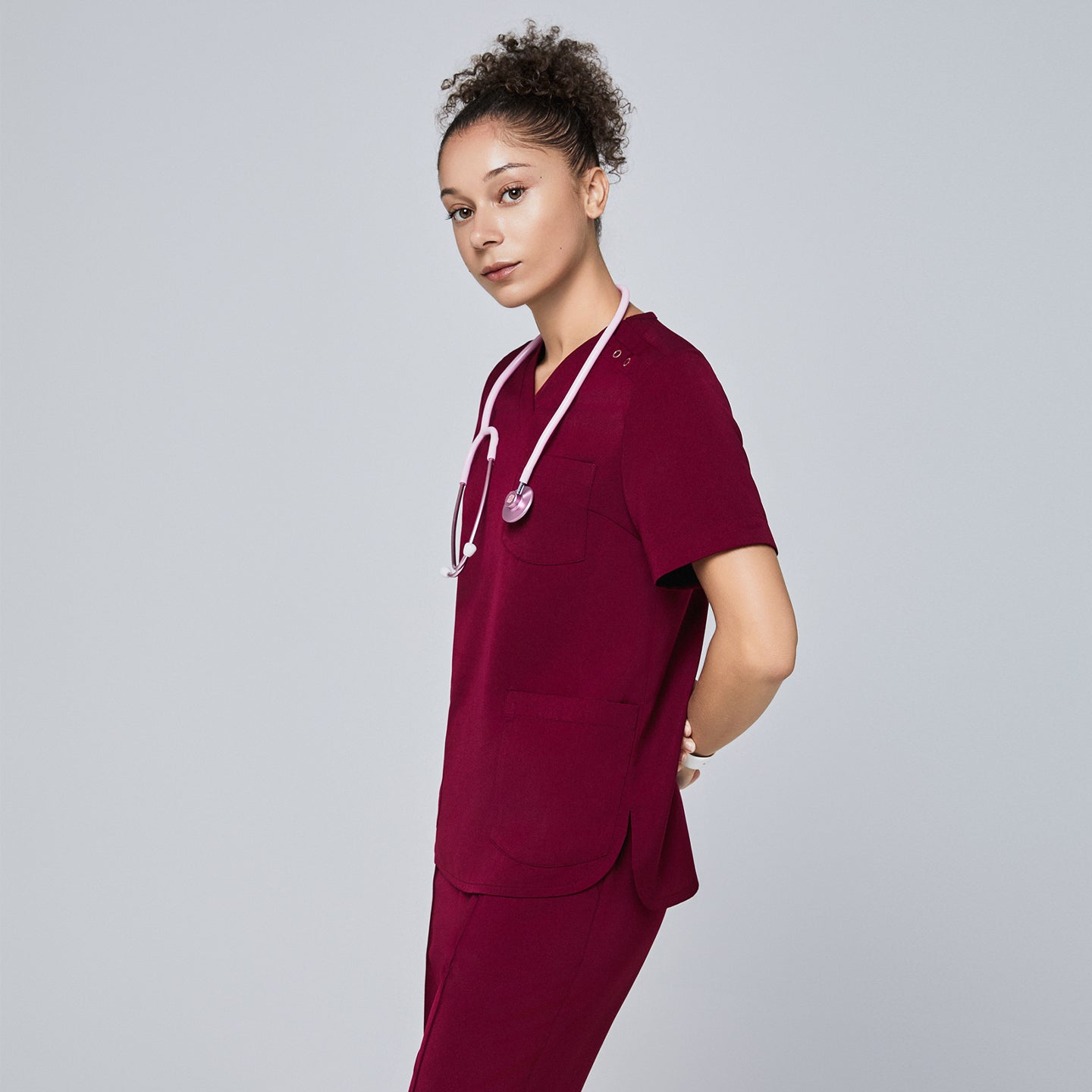 Model in burgundy V-neck scrub top with three-button detail, pink stethoscope, and matching pants,Burgundy