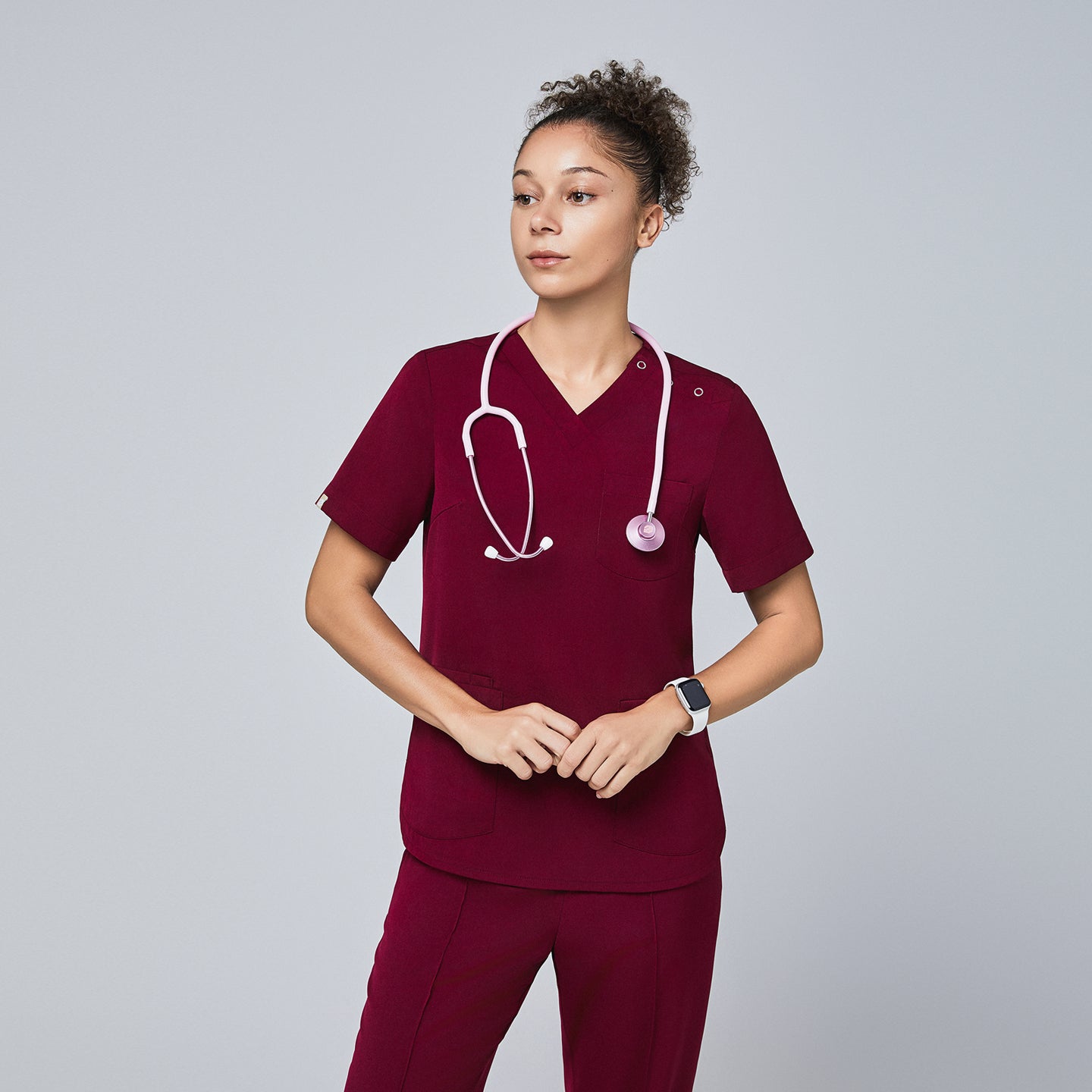 Model in burgundy V-neck scrub top with three-button detail, pink stethoscope, and matching pants,Burgundy