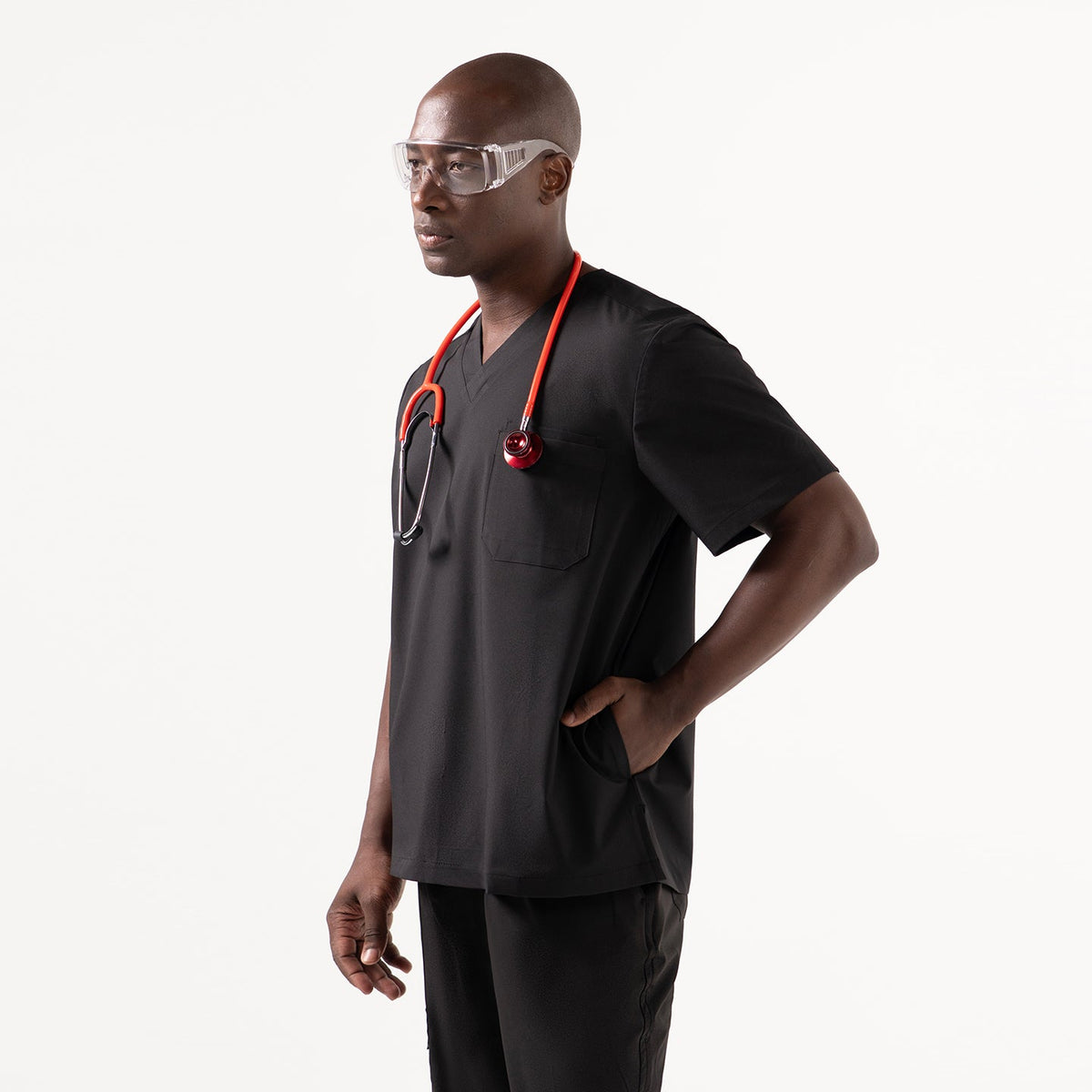 Model wearing an Eco Black V-neck scrub top with three functional pockets, styled with black scrub pants and protective eyewear while holding a confident stance.