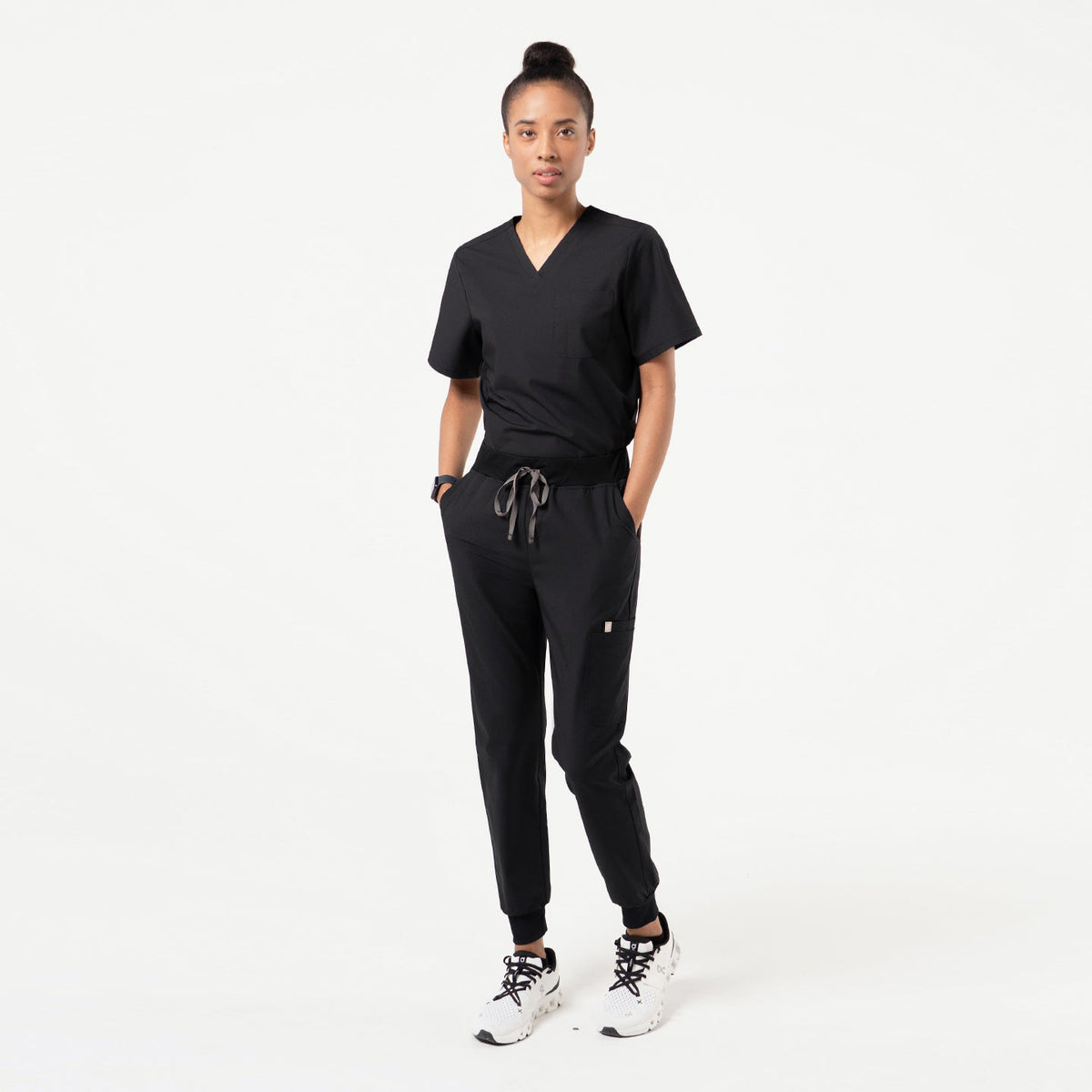 Model wearing Eco-Black jogger scrub pants with back patch pockets and tapered cuffed legs in a minimal studio setting