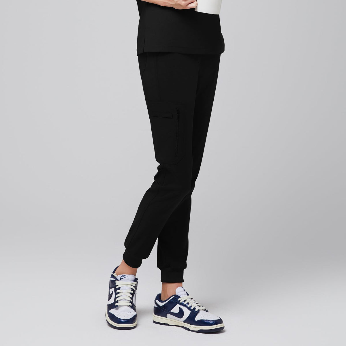 Side view of eco black jogger scrub pants with zipper pocket and elastic cuffs, paired with navy sneakers,Eco Black