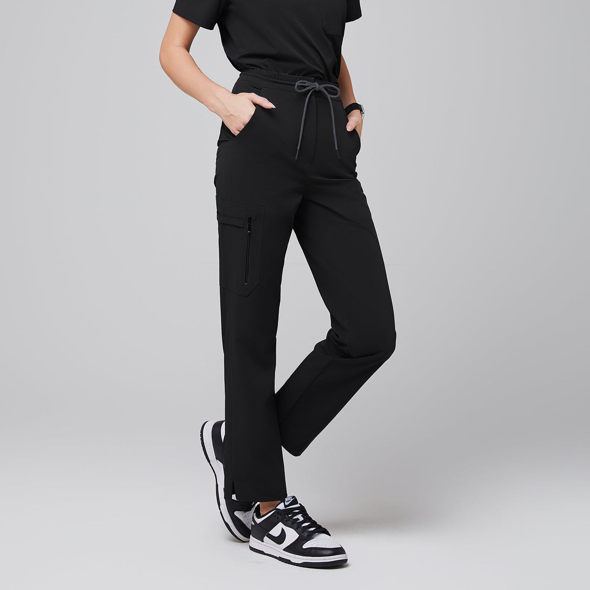 Modern scrub pants featuring a drawstring waist, functional side zipper pocket, and split hem accents, paired with athletic sneakers for a professional yet comfortable look,Eco Black