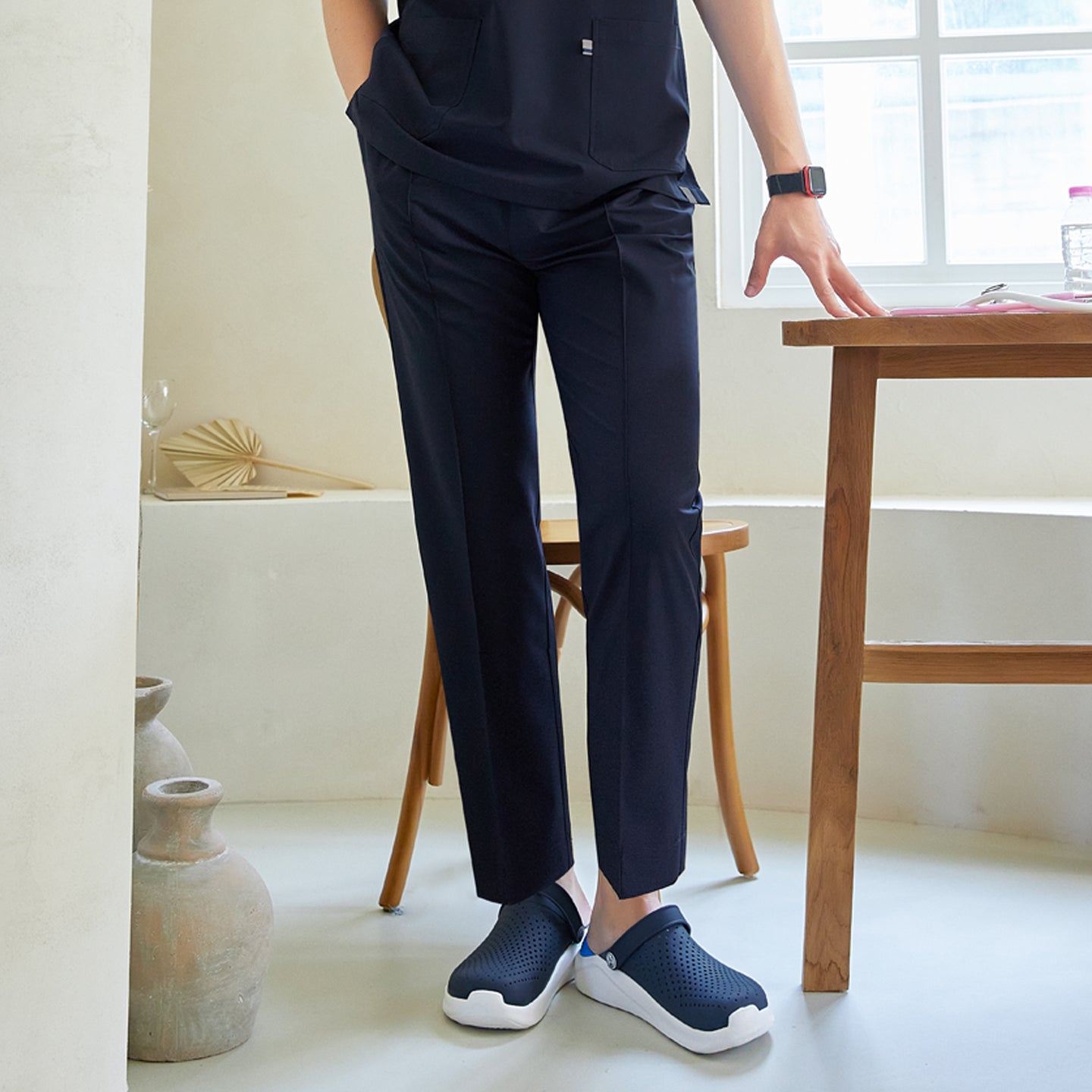 Close-up of man wearing front zipper scrub top with chest and side pockets, paired with straight-leg scrub pants, standing indoors near a table,Eco Navy