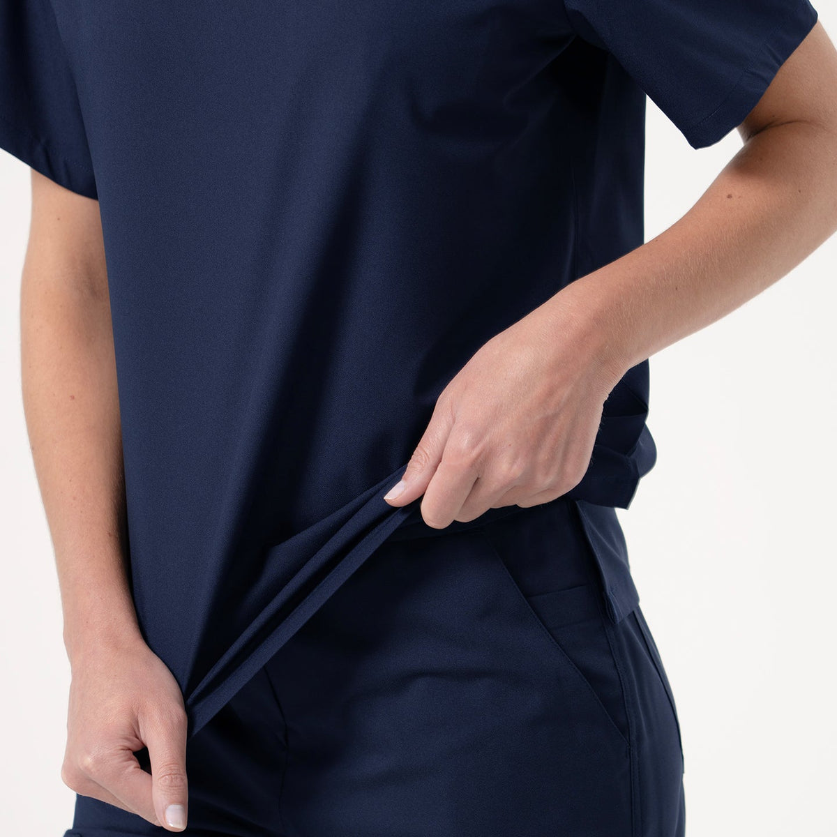 Detail shot of Zenir’s Eco-Navy pleated-shoulder scrub top paired with matching pants, with the model pulling the side of the shirt to emphasize its soft stretch and comfortable fit.