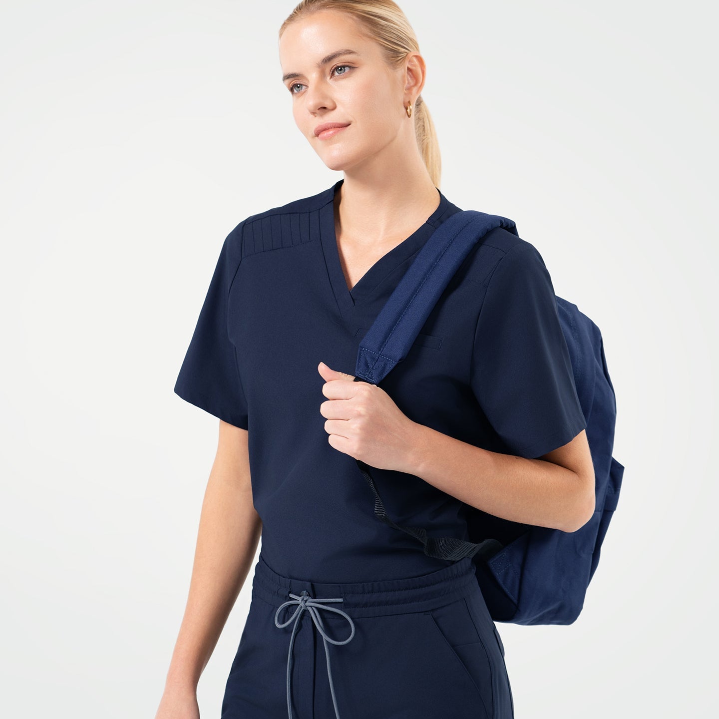 Eco Navy scrub top with chest pocket, paired with matching scrub pants, styled with a navy backpack for a modern professional look.