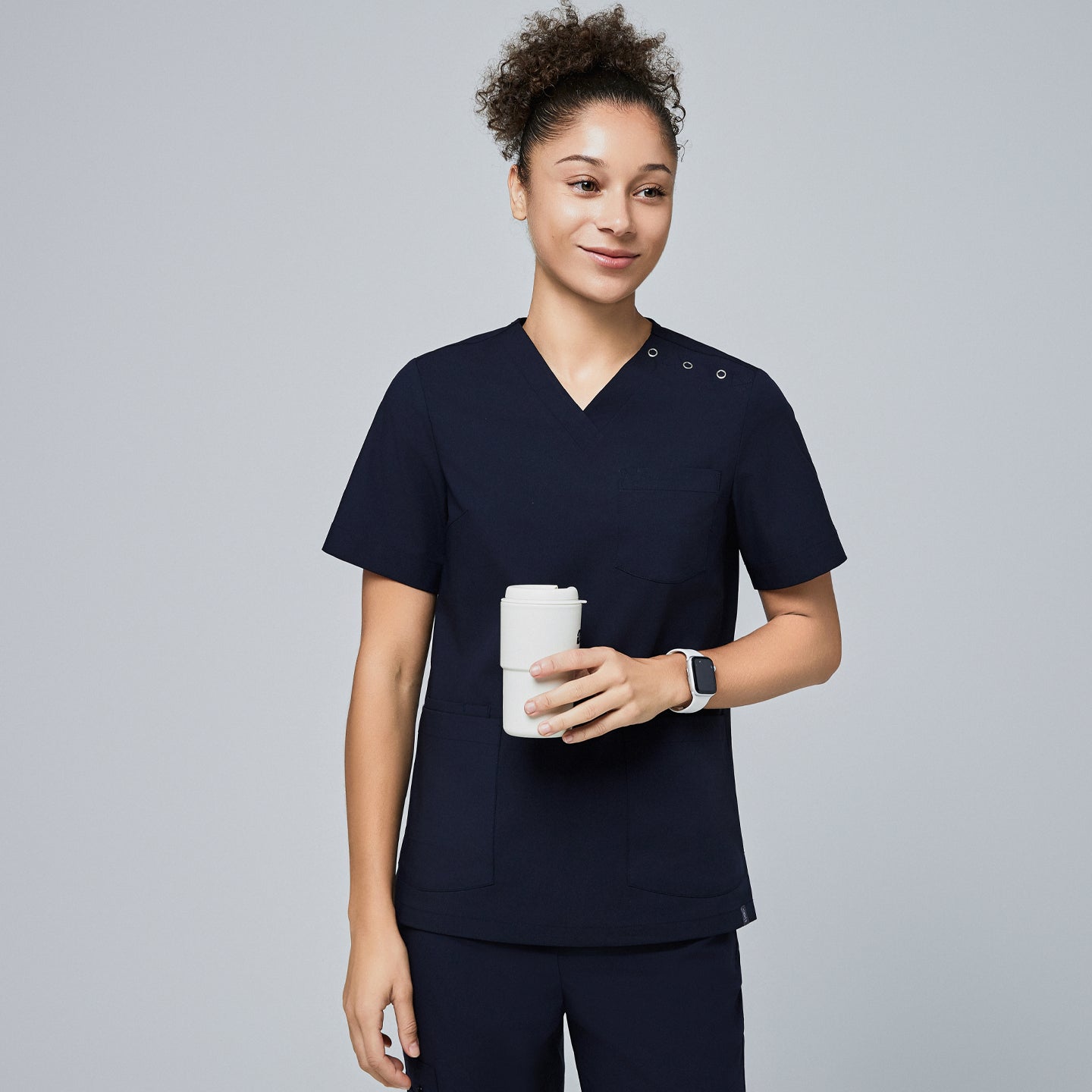 Female model wearing a navy V-neck scrub top with two shoulder buttons and front pockets, holding a reusable coffee cup and smiling,Eco Navy