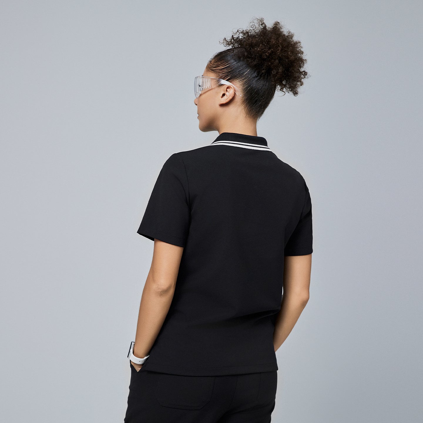 Back view of a woman wearing a black polo scrub top with a white striped collar, paired with black pants,Jet Black