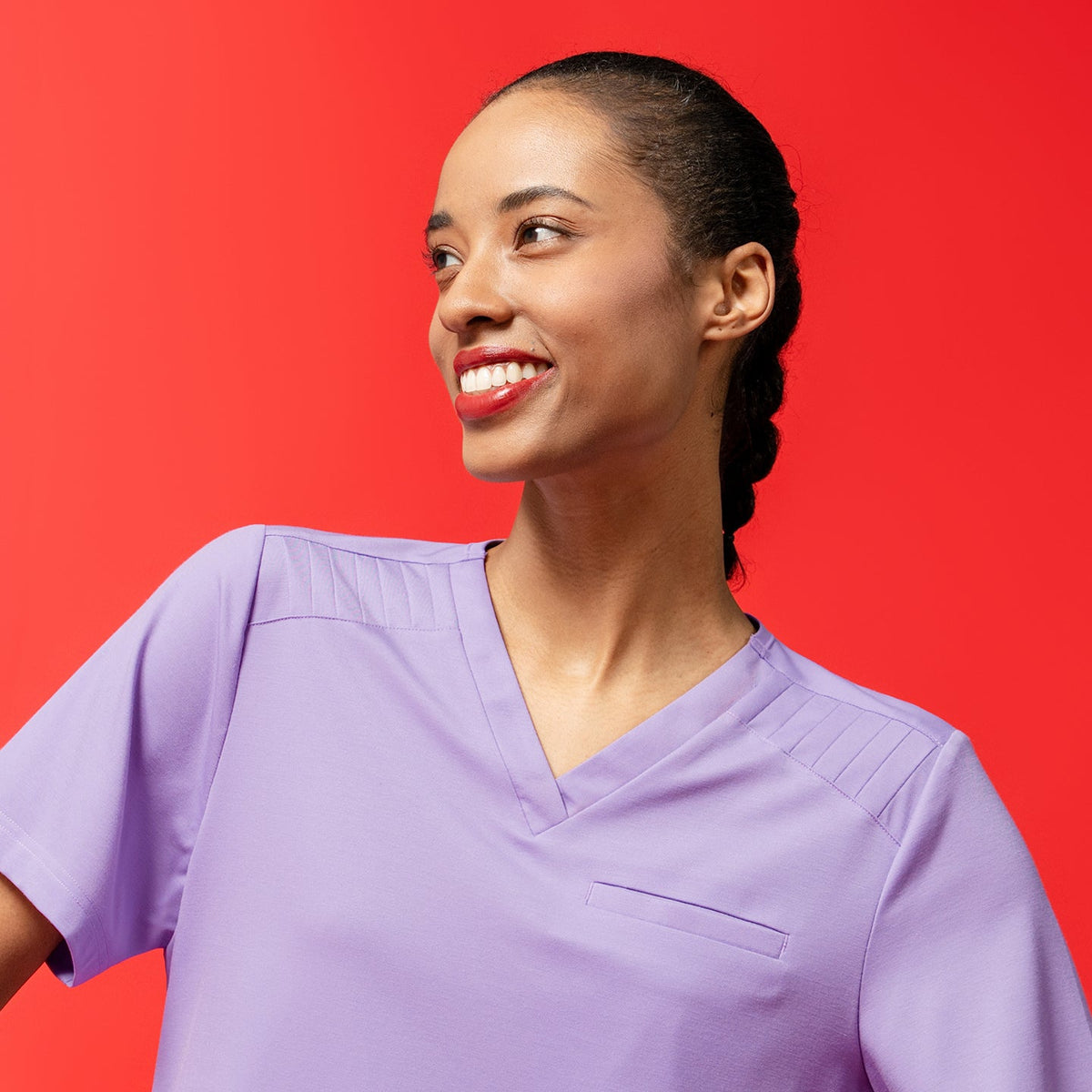 Close-up of the Women's Lavender Pleated Shoulder Scrub Top with pleated shoulder detail, red backdrop, upper body view