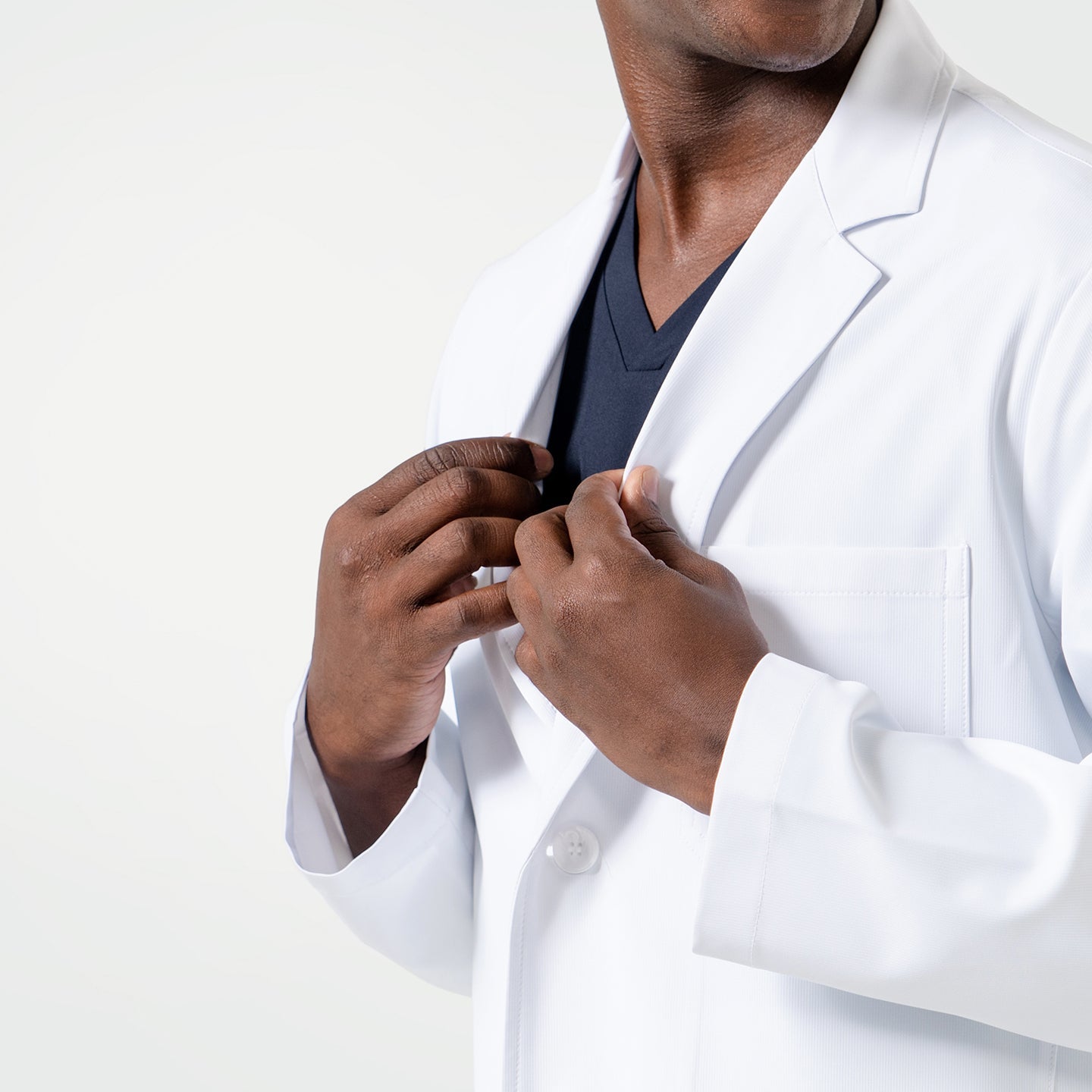 Close-up view of a male model adjusting the LCM-02 White Lab Coat, revealing Eco Navy scrubs underneath.
