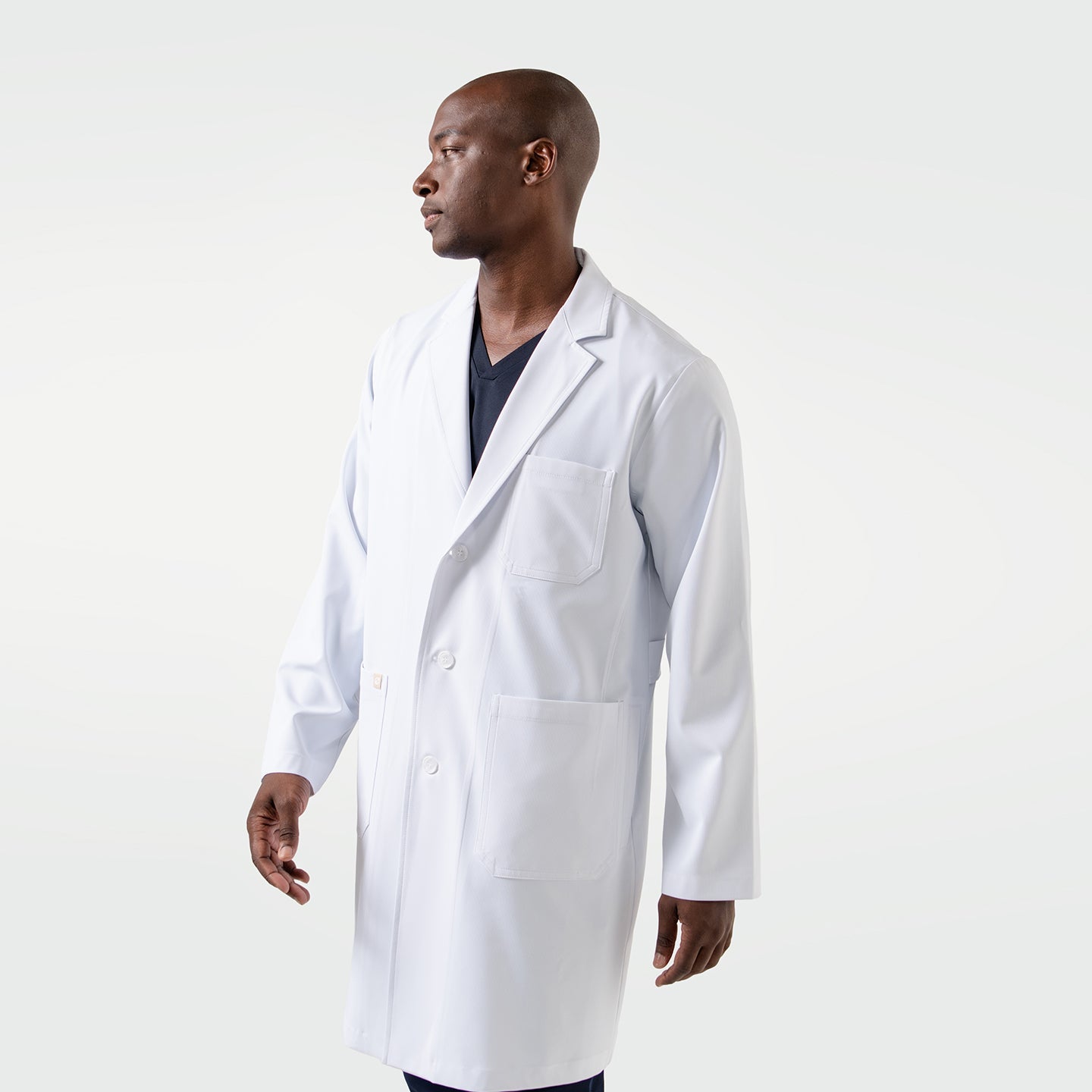 The male model wears the Men’s LCM-02 White Lab Coat over navy scrubs, standing in a side-facing pose with a composed and professional expression.