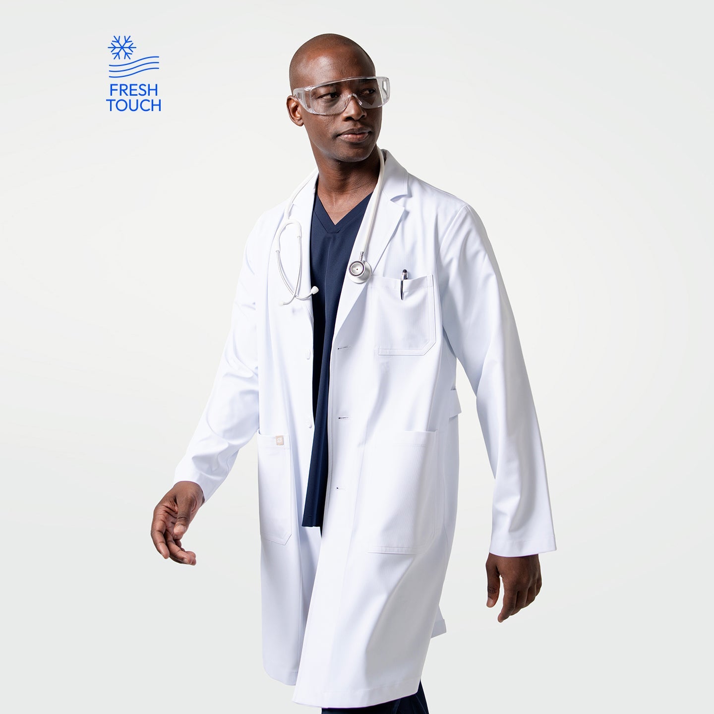 Male model wearing the Men’s LCM-02 White Lab Coat over navy scrubs, accessorized with a stethoscope and clear protective glasses, walking with a confident stride.

