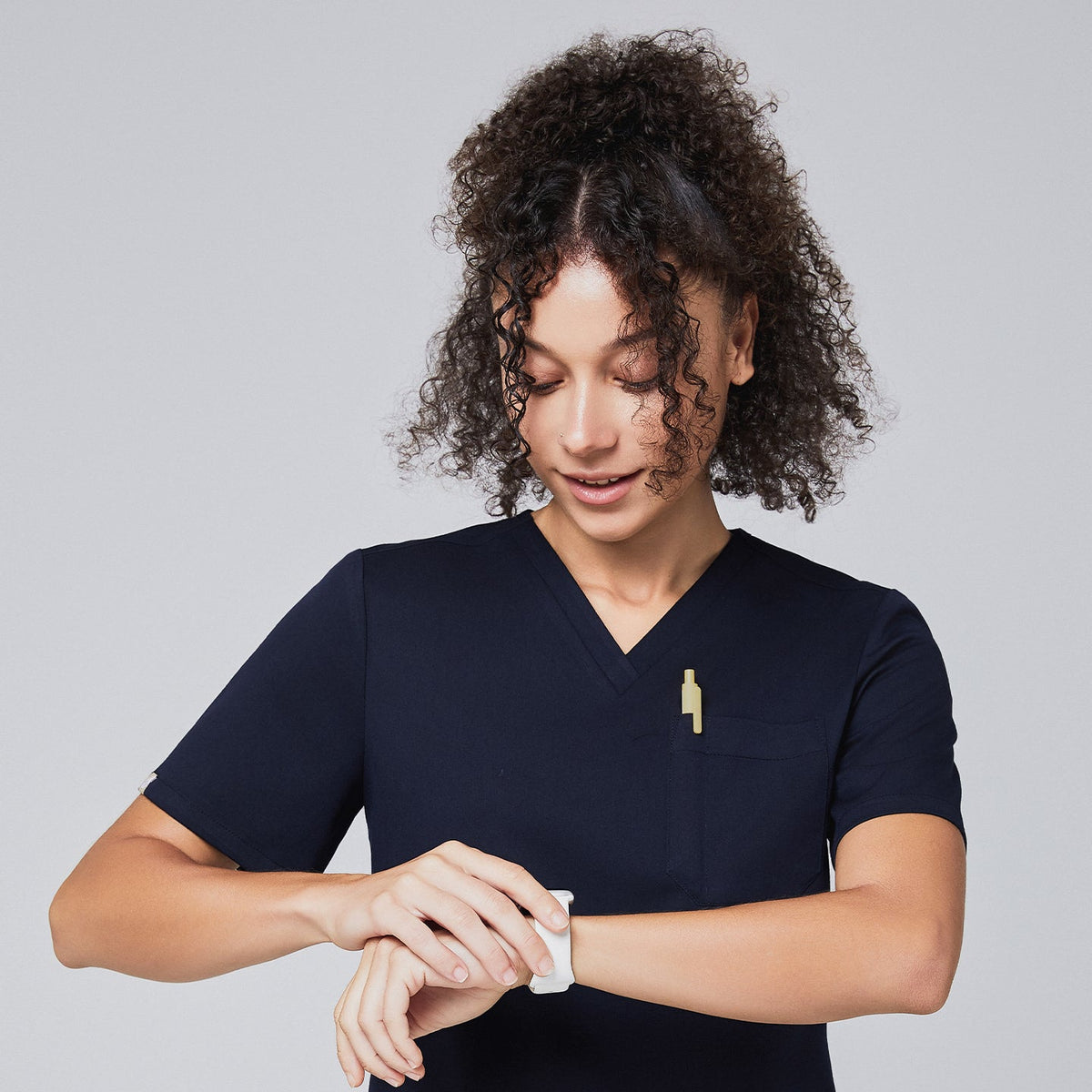 Woman in a navy scrub top checking a smartwatch, with a yellow pen in the chest pocket,Navy