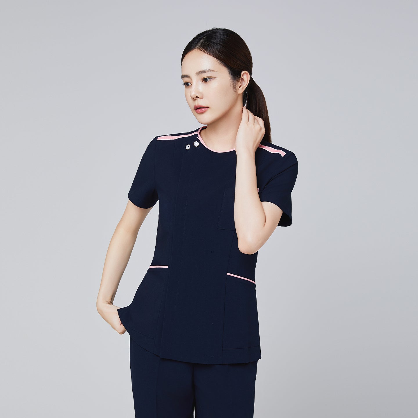Navy scrub top with pink accents and a modern design, featuring a front pocket and short sleeves, modeled by a woman,Navy