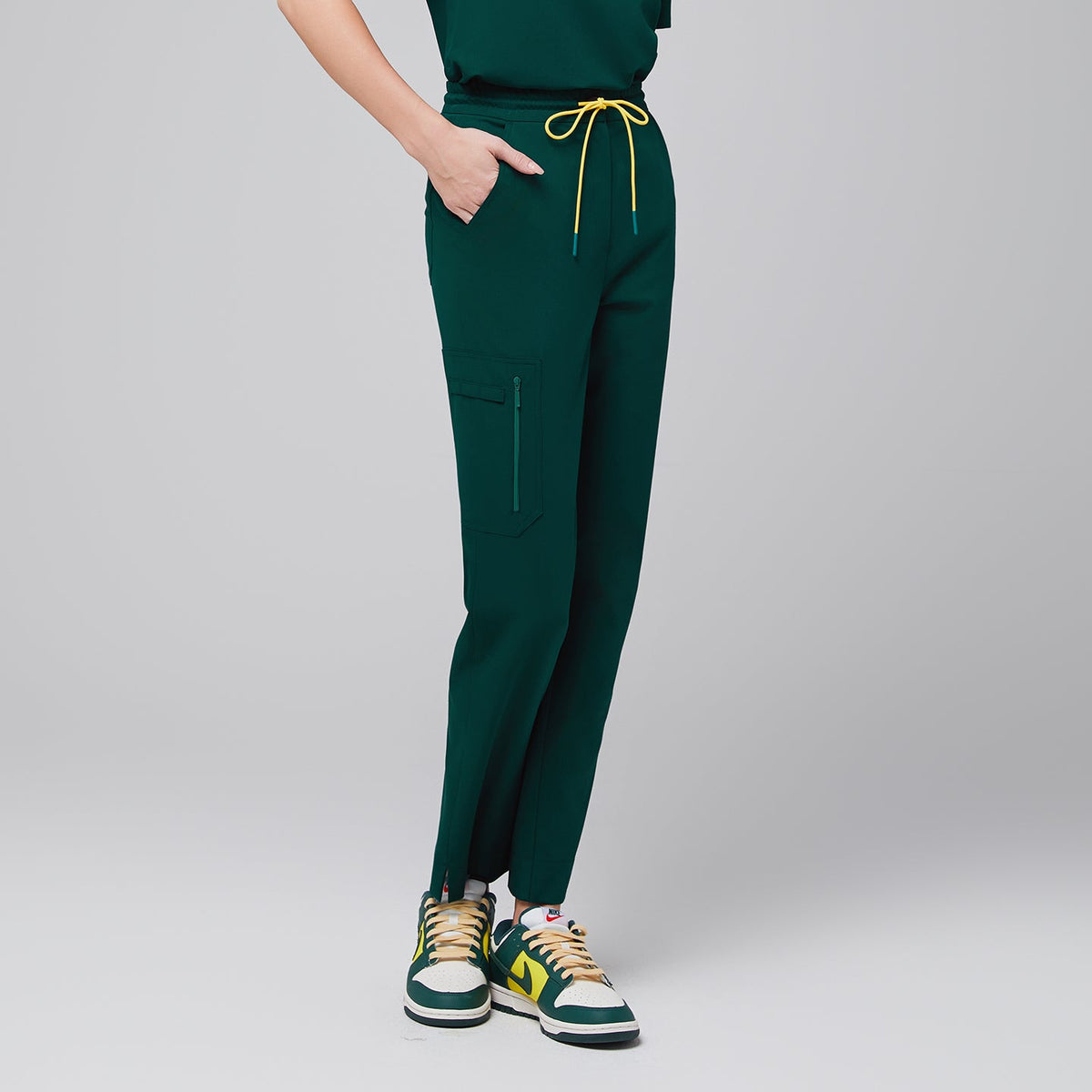 Drawstring scrub pants with a zipper pocket and split hem, styled with casual sneakers for a functional and modern professional outfit,Pine Green