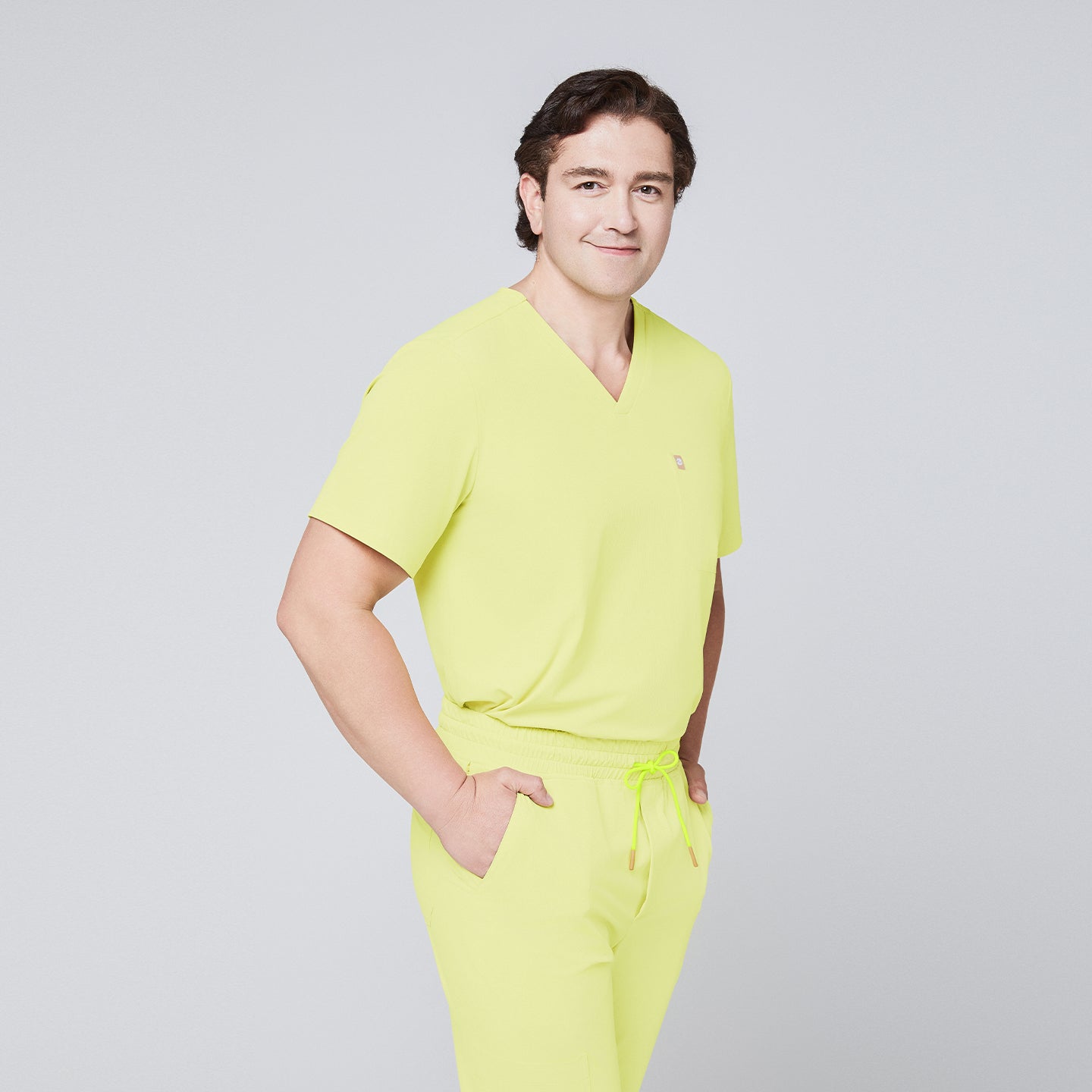 Male model wearing a pineapple yellow V-neck single-pocket scrub top and matching pants, smiling with hands in pockets,Pineapple Yellow