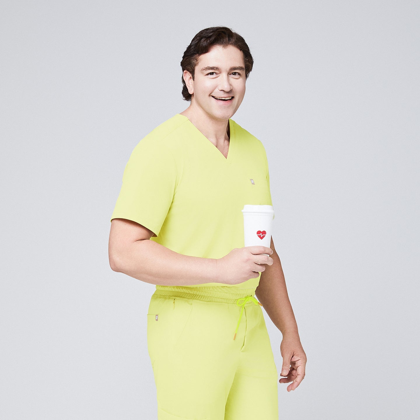 Male model in a pineapple yellow V-neck single-pocket scrub top, holding a coffee cup with a heart design and smiling,Pineapple Yellow