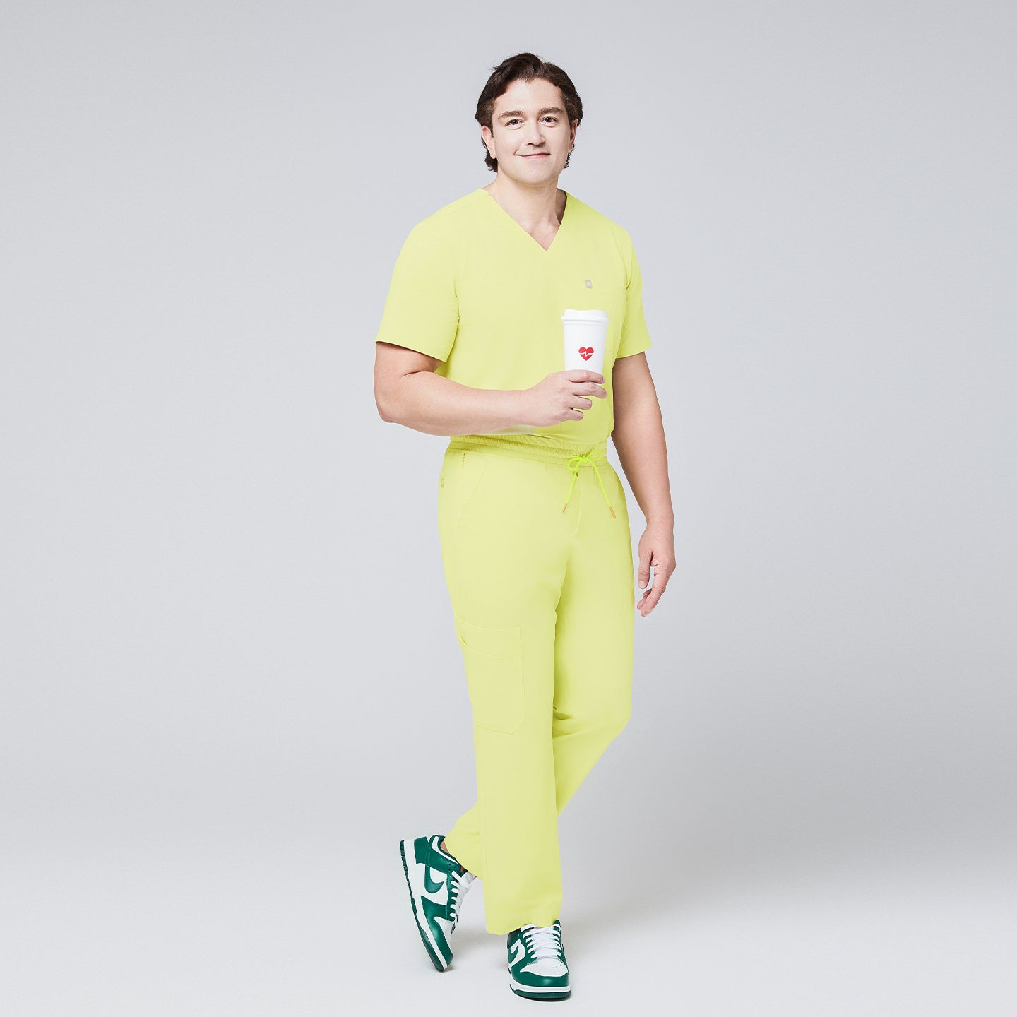 Male model in a pineapple yellow V-neck single-pocket scrub top and matching pants, holding a coffee cup and wearing green sneakers,Pineapple Yellow