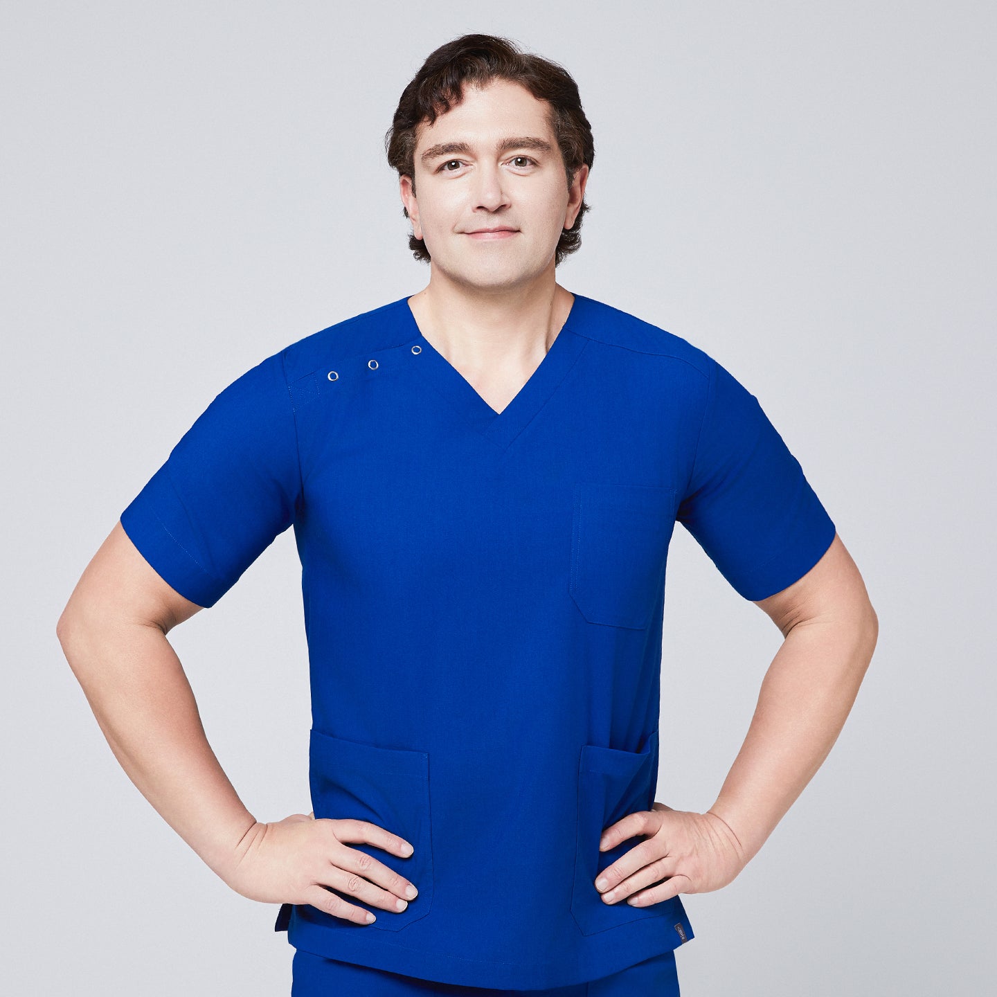 Man wearing Zenir royal blue 3-button scrub top with chest and lower pockets, posing with hands on hips,Royal Blue