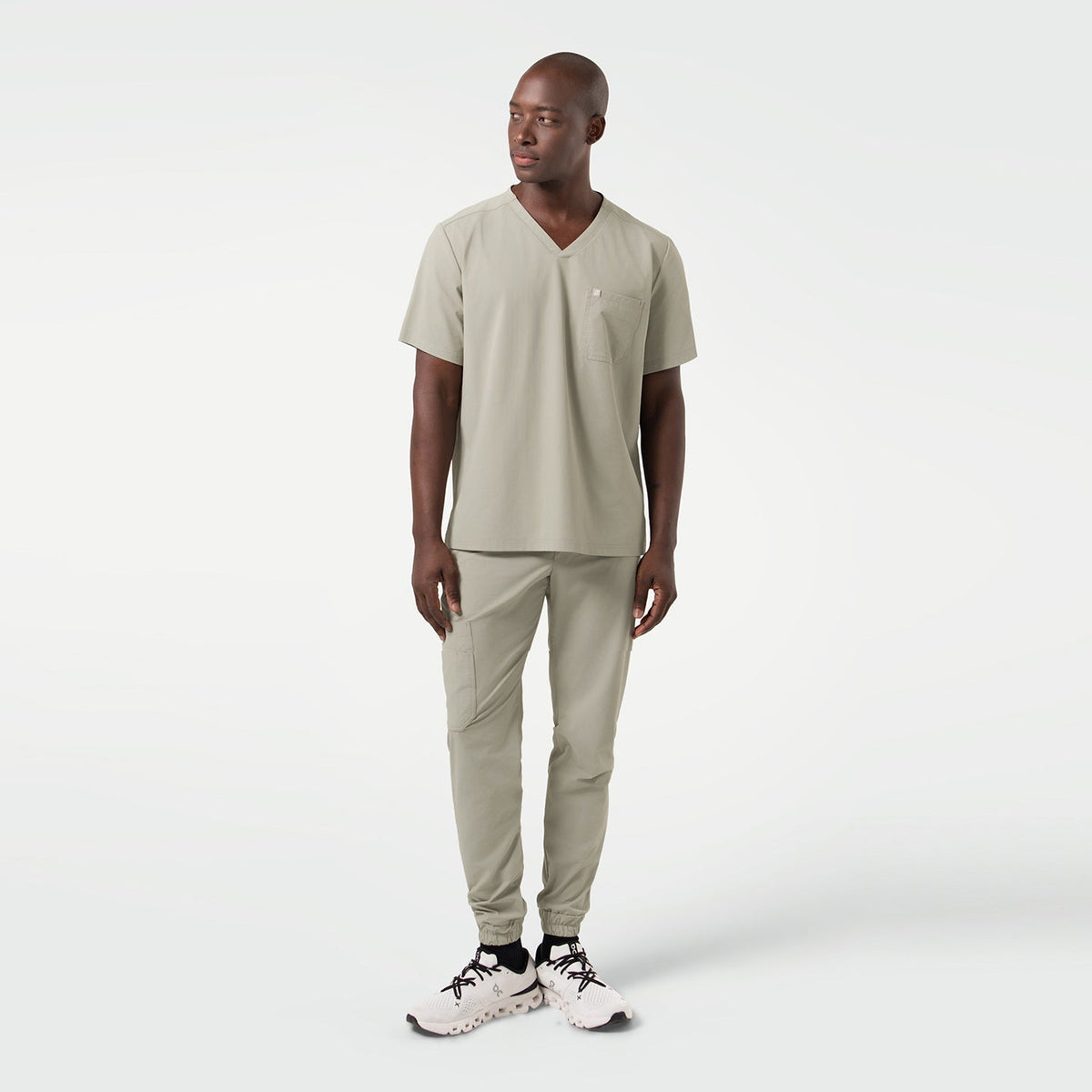 The male model is seen in a full-body shot dressed in Sand Khaki scrubs, standing with a relaxed posture and his gaze directed slightly to the side, showcasing the streamlined fit and contemporary style of the set.