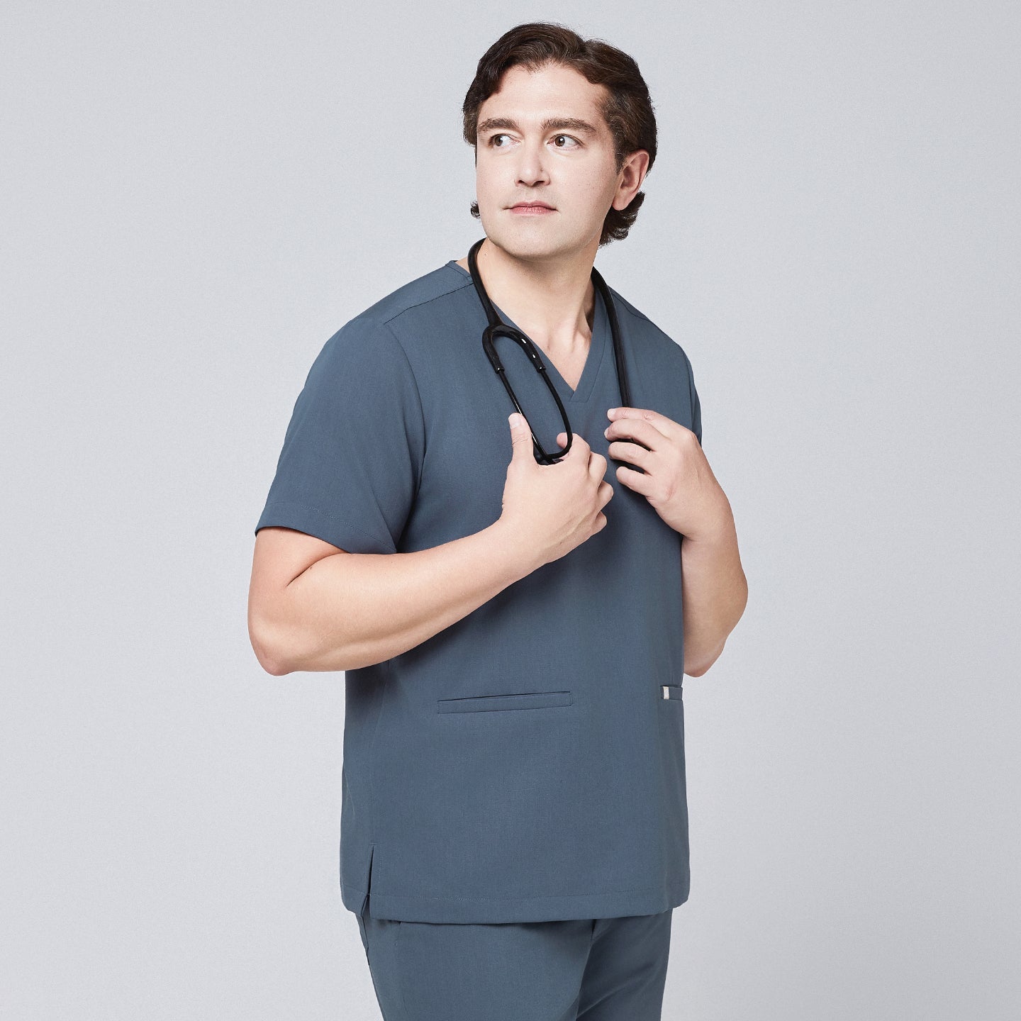 Man wearing a smoky blue scrub set with a double-pocket V-neck top, holding a black stethoscope around his neck,Smoky Blue