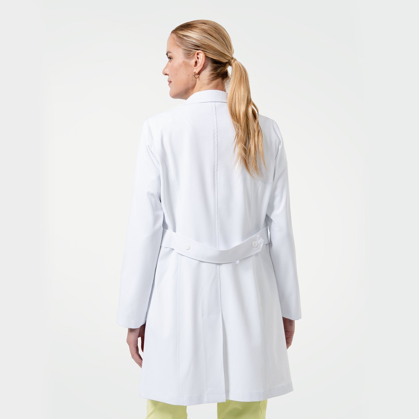 Model wearing a white medical lab coat over yellow scrubs, shown from the back to highlight the coat’s back vent and belt detail on a white background.