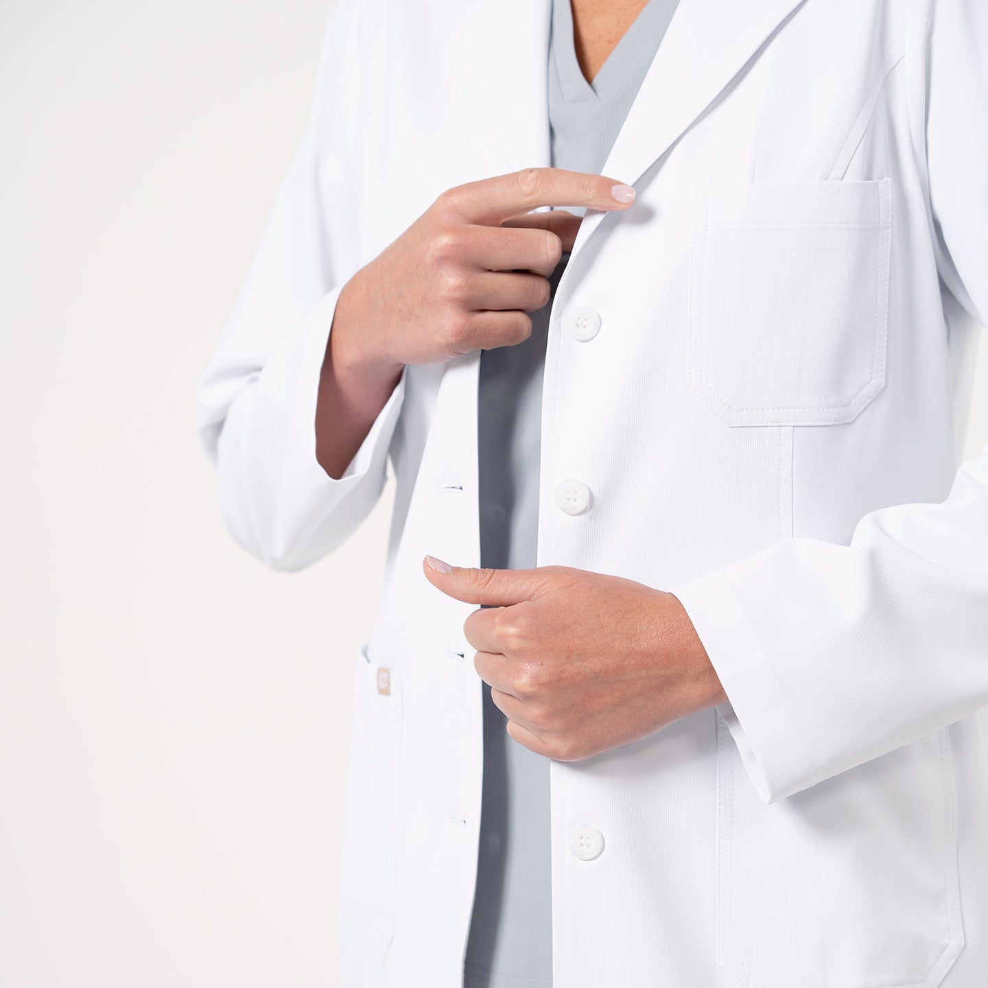 Close-up of the Women’s Long Lab Coat LCW-04 in white, focusing on the chest pocket and front buttons as the model adjusts the coat.
