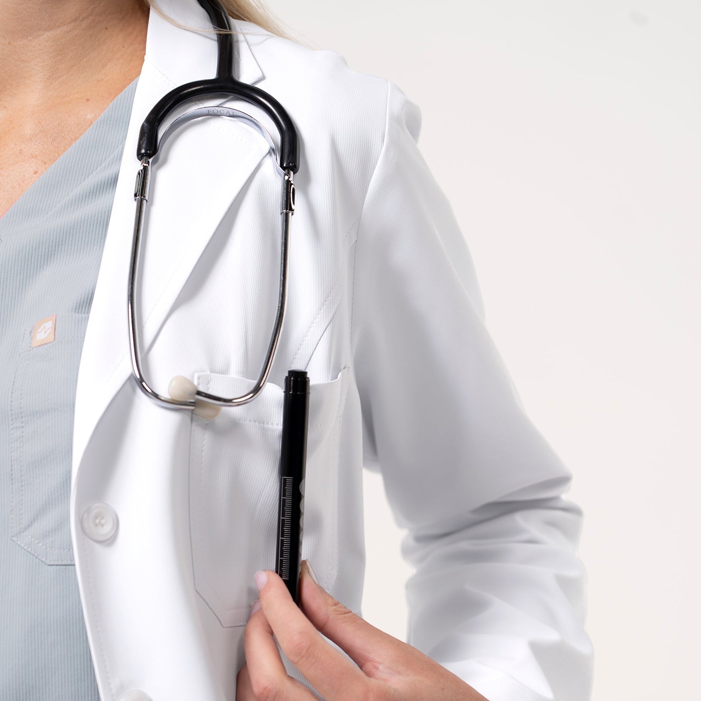 Women’s Long Lab Coat LCW-04 in white, showing the chest pocket holding a pen while the model wears a stethoscope around the neck.