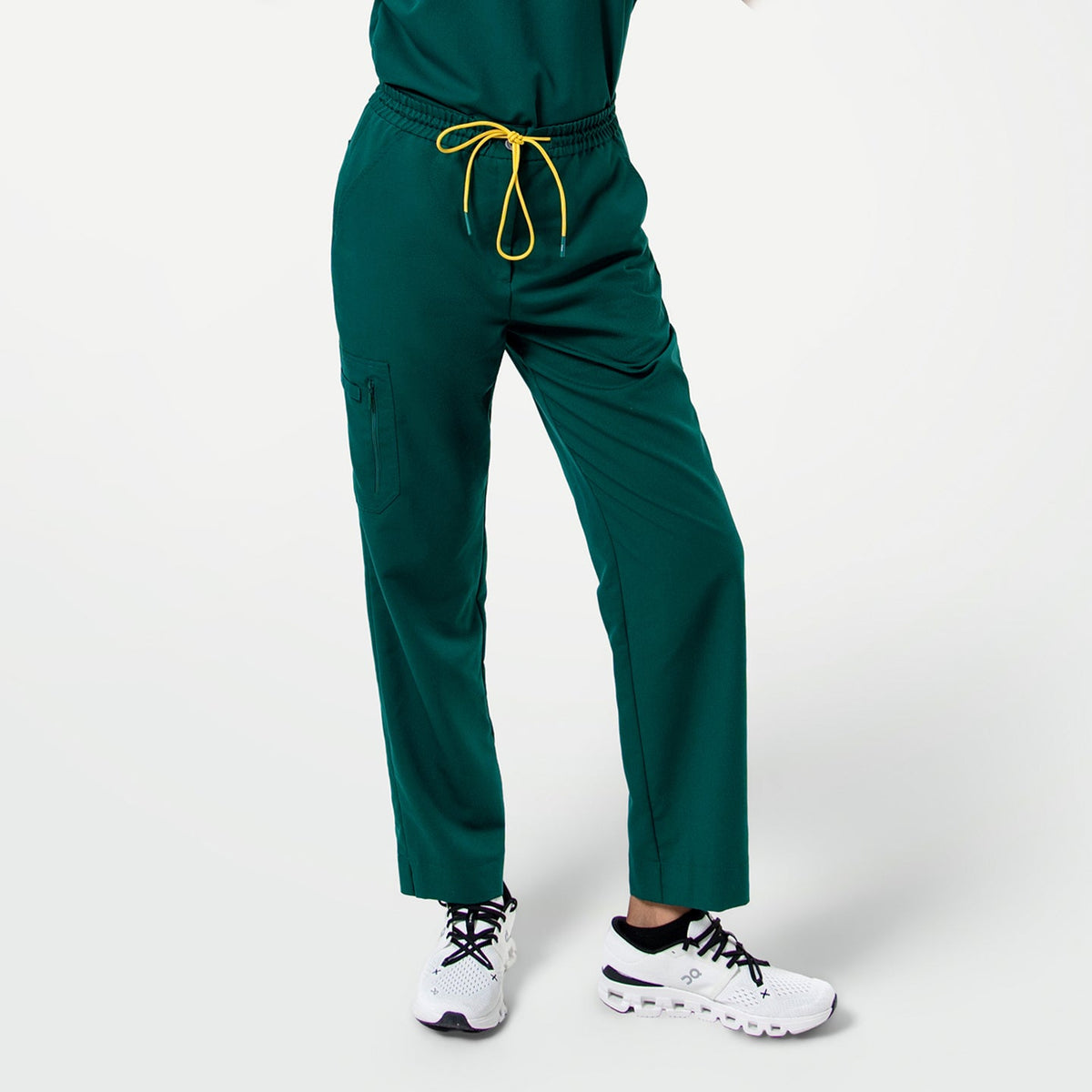 Close-up of Pine Green zipper pocket split hem scrub pants with a yellow drawstring, shown from the waist down.
